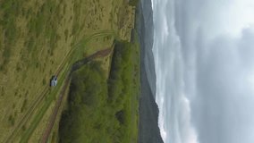 Vertical video footage of the car moves on a country road in a mountainous area. Cloudy summer weather in the forest