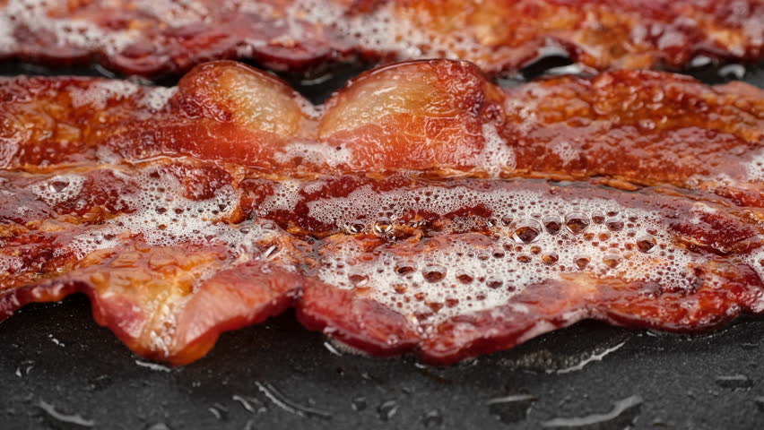 Sliced bacon fried in pan, slider shot