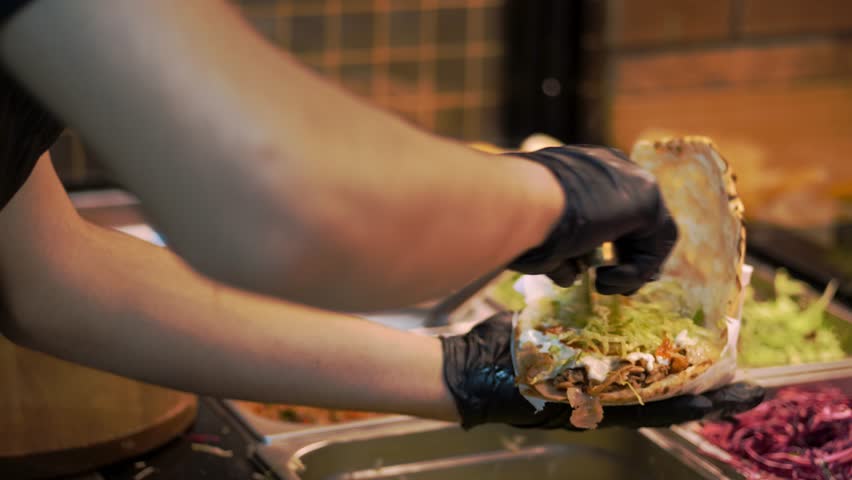 The chef is preparing shawarma using the following ingredients: lavash, meat, sauce, vegetables, cucumbers, onions, cabbage, spicy pepper, potatoes, greens, carrots Royalty-Free Stock Footage #3438470893