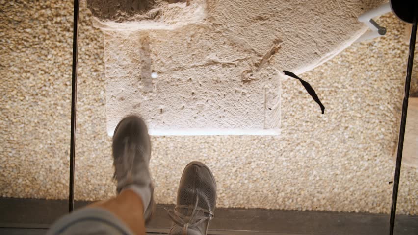 First point view. Museum of archaeological excavations under glass. Historical artifacts. Top view of a tourist's feet walking on a sturdy glass surface. Royalty-Free Stock Footage #3438477429