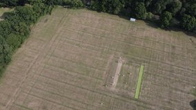 A short aerial film of a cricket match being played on a pitch near some suburban houses