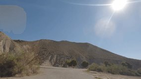 First person view, FPV, from dashcam of car driving in the Tabernas desert in Almeria, Andalusia, Spain. Arid setting of spaghetti western films. Road trip video in POV, with bright, sunny, clear sky
