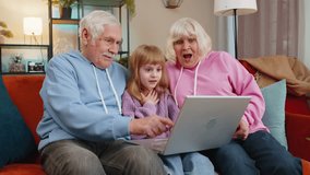Senior Caucasian couple man and woman with child girl granddaughter spending time at home together, sitting on sofa in the living room, using laptop computer. Watching videos playing games on weekend. - Powered by Shutterstock - Get 15% off with code: PIKWIZARD15