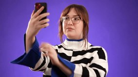 Portrait of happy smiling young woman 20s in sweater taking selfie with mobile cell phone conducting pleasant conversation isolated on purple background studio.