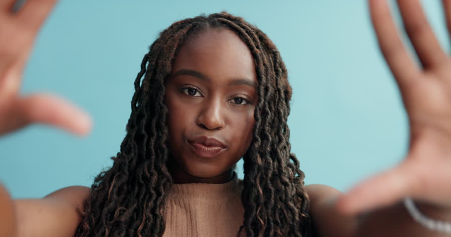 Happy, black woman and hands in frame for photography, picture or selfie in style or fashion on a blue studio background. Portrait of African female person framing face, smile or hairstyle for photo