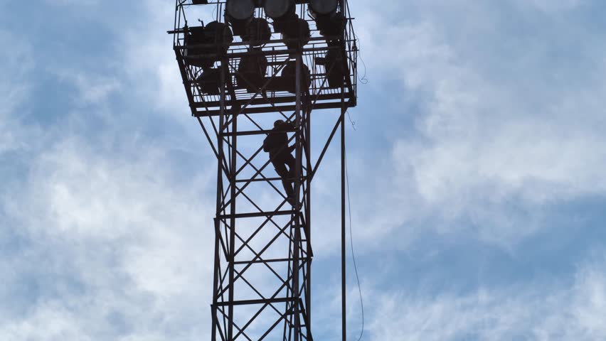 A man climbing an abandoned military watchtower in a rural area. There are many searchlights on the top of the tower. Observation tower Royalty-Free Stock Footage #3438710907
