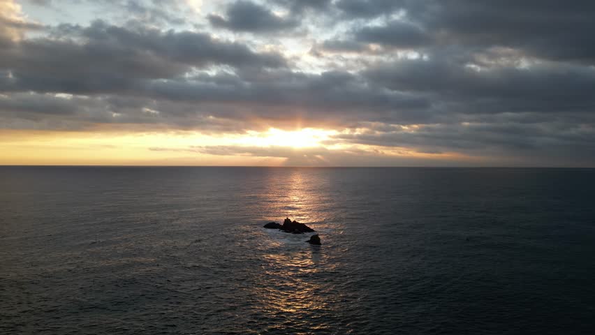 Sunrise over Costa Brava, Spain, with sunbeams piercing through clouds onto the serene Mediterranean Sea and isolated rock formations.