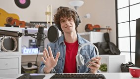Hispanic man with curly hair reviews headphones in a modern music studio, creating engaging content.
