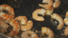 Close-up of shrimps being fried in a frying pan in oil with garlic, stirring them. Macro food background