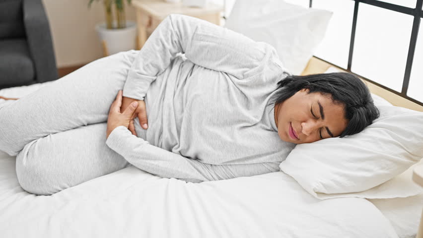 Mature hispanic woman in pain lying in bed at home, clutching her stomach. Royalty-Free Stock Footage #3438791991