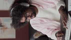 Vertical waist up of young Biracial male freelance interior designer in headphones sitting at desk by computer, typing while creating 3d rendering - Powered by Shutterstock - Get 15% off with code: PIKWIZARD15