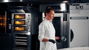 A girl baker in a jacket and gloves claps her hands with flour in a professional kitchen in a bakery - Powered by Shutterstock - Get 15% off with code: PIKWIZARD15