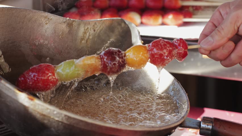 Making fruits in boiling caramel close-up. Chinese winter sweet dessert Tanghulu street food.Berries, grapes, tangerine and others fruit caramelized in sugar. Asian street market with traditional food