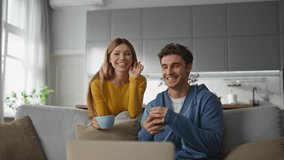 Overjoyed spouses waving hands talking laptop emotionally. Relaxed couple sitting couch sipping tea at domestic weekend. Joyful laughing pair having fun telling stories to friends at video call - Powered by Shutterstock - Get 15% off with code: PIKWIZARD15