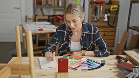 Blonde woman in a flannel shirt engaging with a color palette and smartphone at a carpentry workshop.
