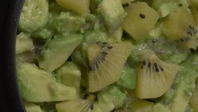 Close up view of homemade avocado chunky guacamole with yellow kiwi fruit in a bowl. Table spin. Vertical video.