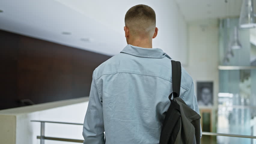 A confident young man with a backpack standing in a modern university library