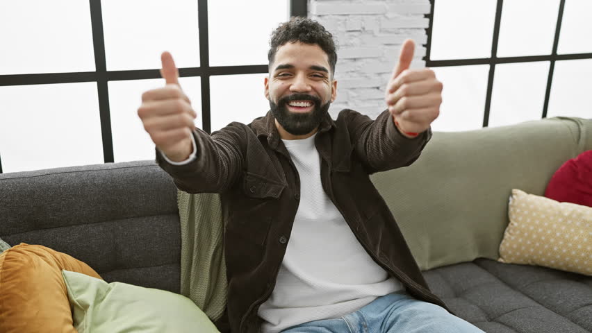 Cheerful young man opening his arms wide for a hug, a beacon of happiness and warmth, smiling at the camera - all from the comfort of his cozy living room at home