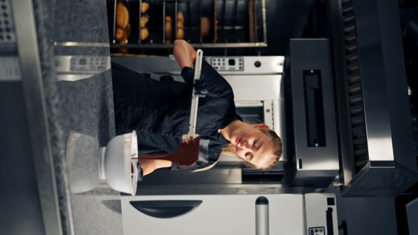 Girl chocolatier using a silicone spatula mixes chocolate for making desserts in a pastry shop