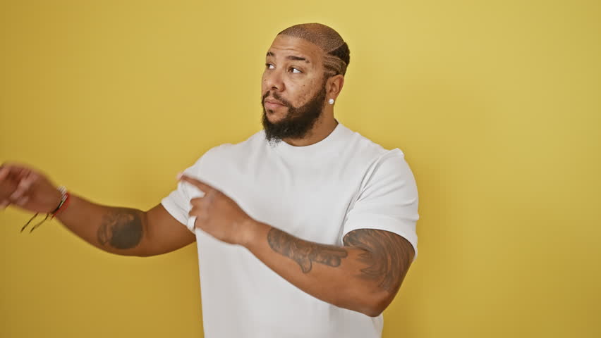African american man standing smiling and looking at the camera pointing with two hands and fingers to the side. over isolated yellow background