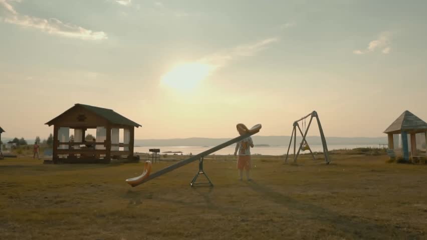 Girl child in the park plays with a swing. A chidhood dream. Girl playing in park. Happy girl playing. Playground in the park on the lake in the campsite. Summer, autumn vacation. Warm weekend