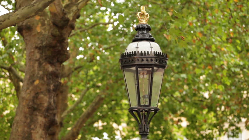Close up of top of street light with green trees in background in London,