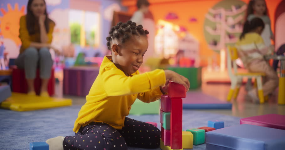 Cheerful African Girl Playing with Colorful Building Blocks in Kindergarten. Beautiful Black Child Posing, Looking at Camera and Smiling. Happy Children Playing in Modern Daycare Center Royalty-Free Stock Footage #3439062625
