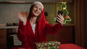 A cheerful young woman in a festive Santa hat engages in a virtual holiday greeting via a video call, surrounded by Christmas decorations. - Powered by Shutterstock - Get 15% off with code: PIKWIZARD15