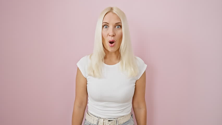 Hilarious blonde young woman standing over isolated pink background, puffing cheeks in a crazy funny face expression, making air puff with mouth - confident yet amusing! Royalty-Free Stock Footage #3439070321