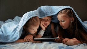 children covered with a blue blanket looking at a tablet. High quality 4k footage