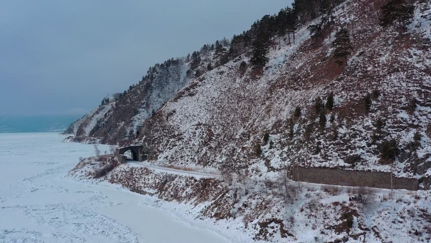 Aerial drone view tunnels and bridges winter circum-Baikal railway at the foot of the mountains on the coast of Lake Baikal, Siberia, Russia. High quality 4k footage