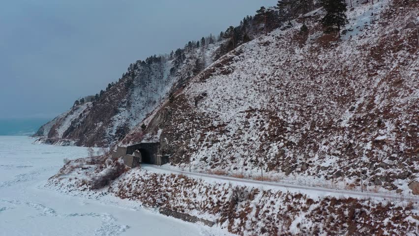 Aerial drone view tunnels and bridges winter circum-Baikal railway at the foot of the mountains on the coast of Lake Baikal, Siberia, Russia. High quality 4k footage Royalty-Free Stock Footage #3439221659