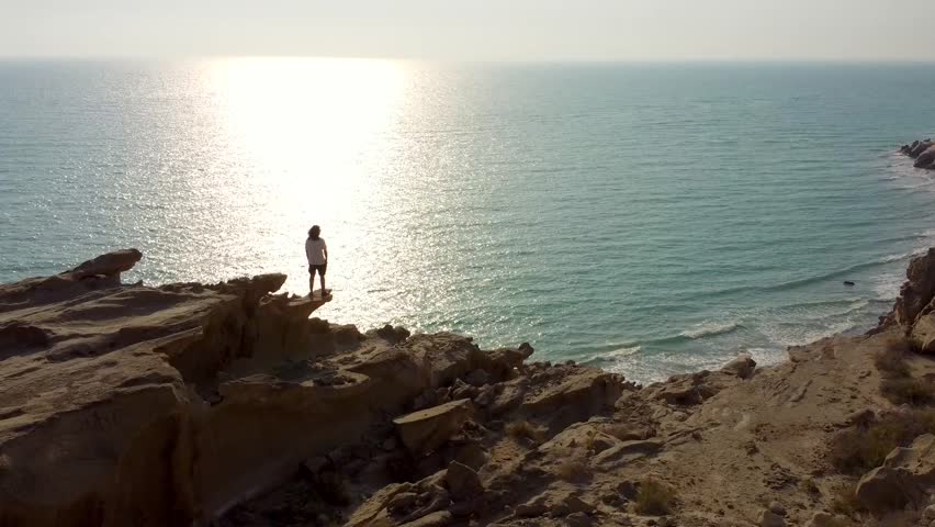 a man stand alone on sea side high rock cliff beach in sunset time a wide view of ocean harbor coastal lake sun reflection in Hormuz Island Qeshm district local people lifestyle tropical climate Iran
