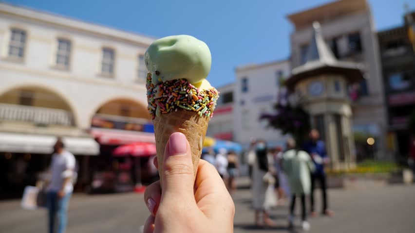 Tourist woman holds cone of ice cream, clip capturing the tempting and flavorsome delight against blurred view of Buyukada clock square.