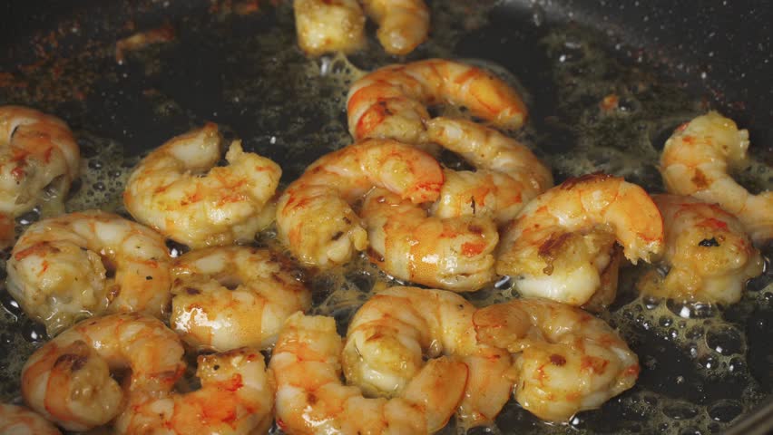 Shrimps are fried in a frying pan in oil with garlic, stirring them. Close-up Royalty-Free Stock Footage #3439547547