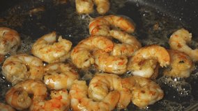 Shrimps are fried in a frying pan in oil with garlic, stirring them. Close-up