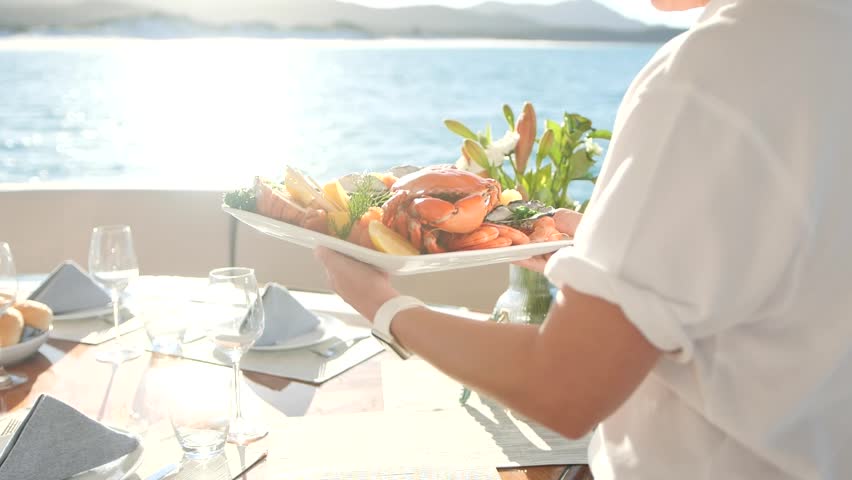 Waitress serving a fresh seafood platter on a sunny ocean deck. Royalty-Free Stock Footage #3439615931