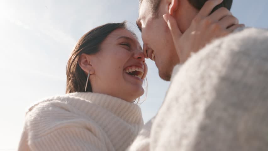 A smiling young couple in cozy sweaters embracing under the clear sky. The joy and affection between them are palpable, epitomizing pure happiness and love. Royalty-Free Stock Footage #3439669153