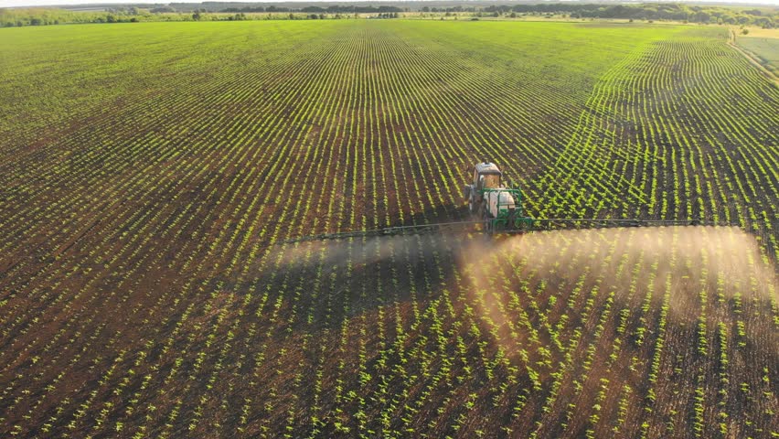 Aerial video of tractor spraying soil and young crop in springtime in field. Tractor spraying pesticides on soy field with sprayer at spring. Nozzle of the tractor sprinklers sprayed, growth concept. Royalty-Free Stock Footage #3439757849