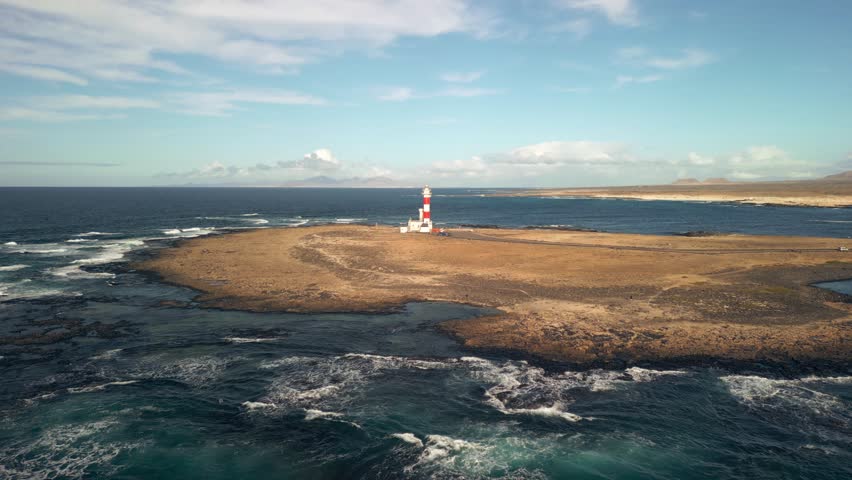 The 19th century red and white bands Faro del Tostón lighthouse located on the northwest coast of Fuerteventura in the Canary Islands. A lighthouse against the background of the blue sky and the ocean