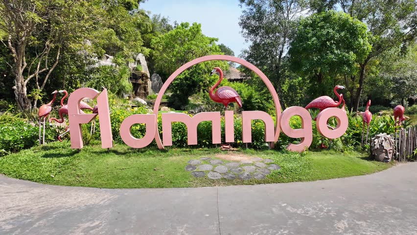 Vibrant flamingo sculpture and signage at a tropical park on a sunny day, perfect for wildlife and nature themed design projects or tourist attraction promotions