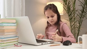Virtual classroom interaction. E-learning environment for kids. Serious Caucasian little brown haired girl using laptop studying online at home writing down information with focused expression