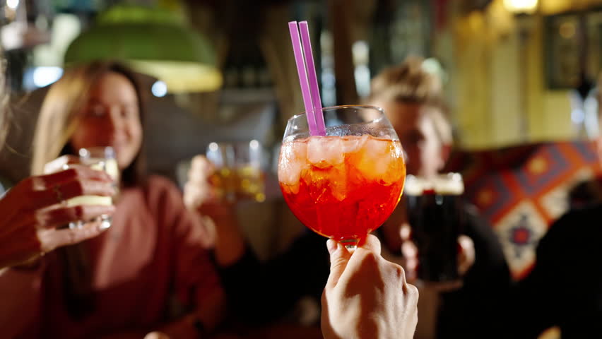 Young people cheers alcohol drinks. Friendship, togetherness concept. Group of happy multiethnic friends having fun together, drinking bottled beer in a bar or at home, celebrating, happily smiling.