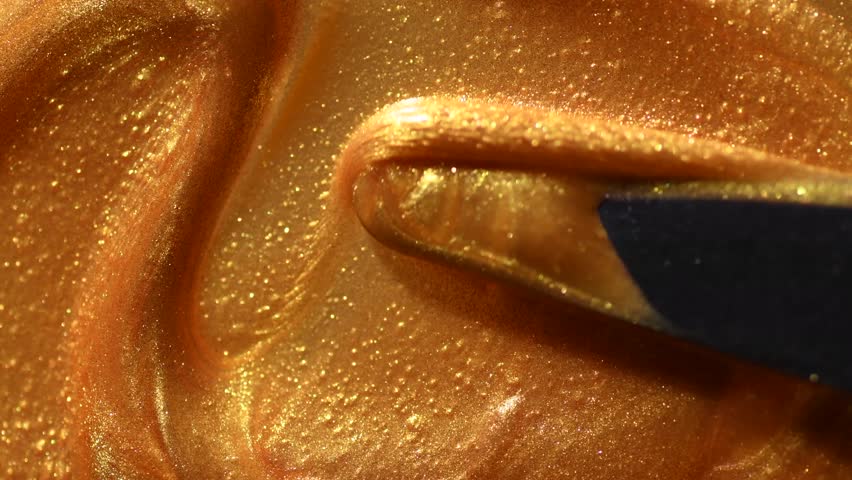 Golden smear of liquid gold paint texture background mixing by palette knife. Painting Gold metallic paint close-up. Liquid gold Art design backdrop. Leaking Lipgloss, nail polish, make-up backdrop 