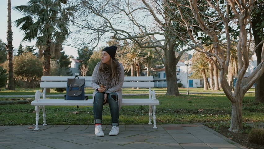 Young woman using  phone in a park with palms in the autumn or winter time
