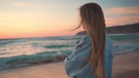 Relaxed woman with blond windswept hair enjoying beautiful sunset over ocean. Smiling young female lady in denim shirt looking at camera on shore near sea waves. Caucasian girl enjoying vacation. - Powered by Shutterstock - Get 15% off with code: PIKWIZARD15