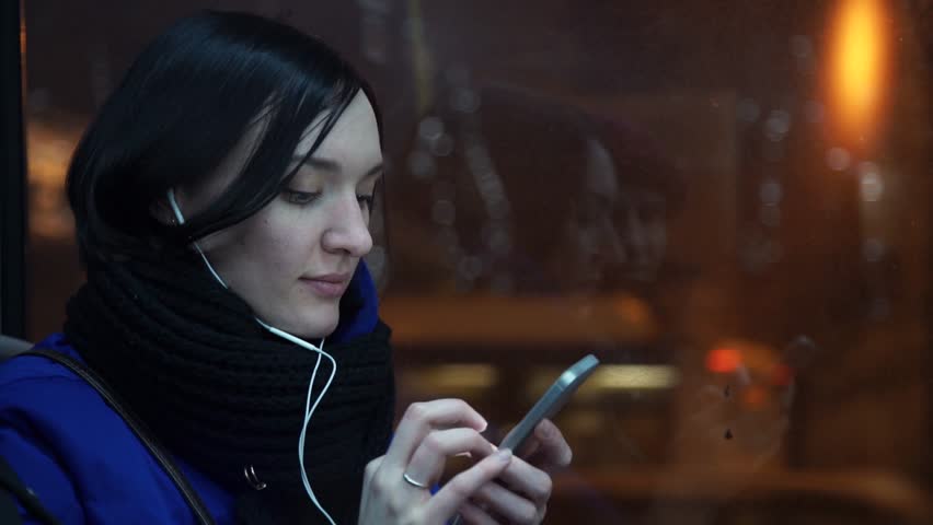 Portrait of young girl listening music with headphones using smart phone during bus ride in evening in city. Car traffic on background. Slow motion Royalty-Free Stock Footage #34399627
