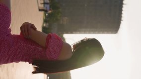 Portrait of a Young Adult Brunette Woman Wearing Glasses and a Pink Dress on a City Background in Sunset Light. Concept of Spring Time and World Women's Day. Vertical Video, Slow Motion.