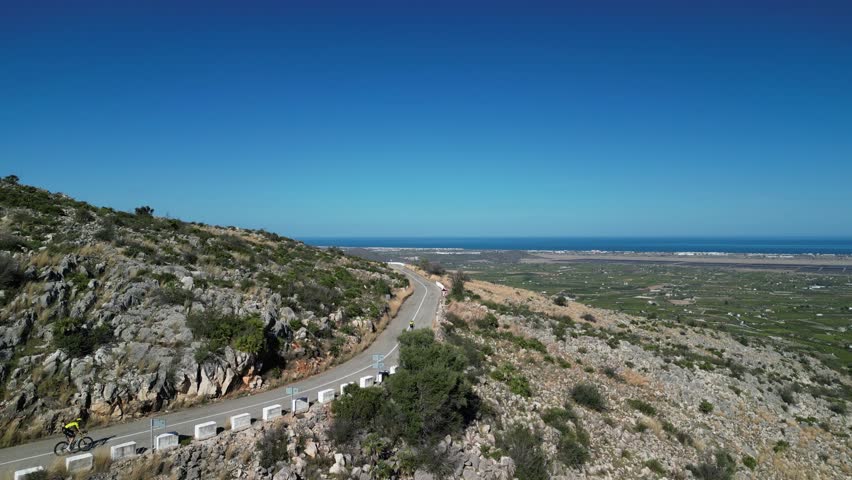 Aerial drone footage of group cyclists riding down hill on winding road. Cycling and triathlon concept. Athletes training on bicycle. La Vall d