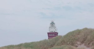 This stock footage beautifully captures a serene lighthouse emerging from behind the gentle dunes of a coastal landscape. The scene is enveloped in a soft, diffused light, creating an atmosphere of